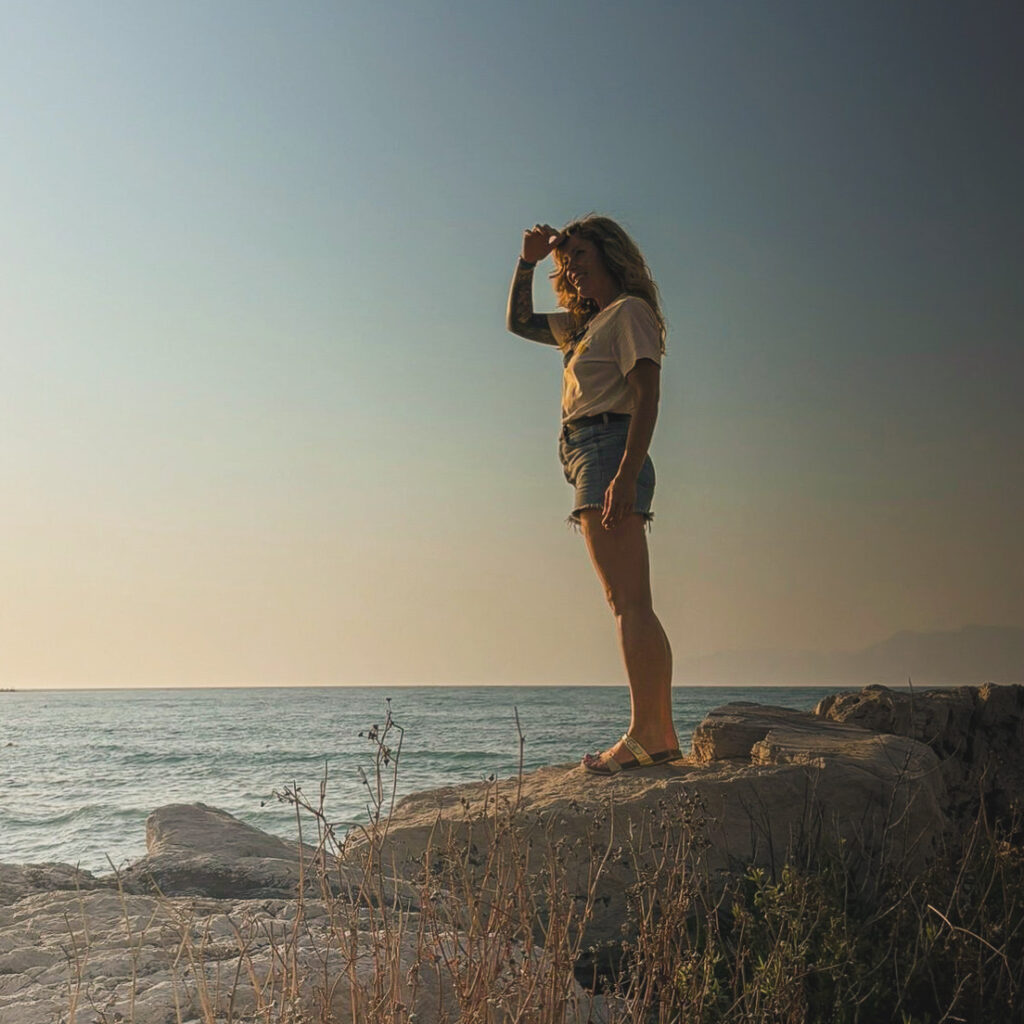 Frau auf Felsen am Meer bei Sonnenuntergang