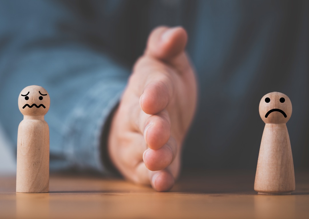 Konflikt - Hand zwischen zwei Spielfiguren mit traurigen Gesicht